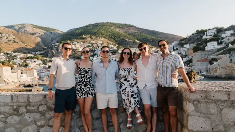 A group of young travellers posing at sunset in Hydra during a MedSailors Greece island hopping sailing holiday, with the town and hills in the background.