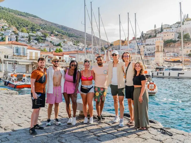 A group of young travellers posing at a picturesque marina, experiencing an unforgettable yacht sailing adventure through Greece’s iconic islands.