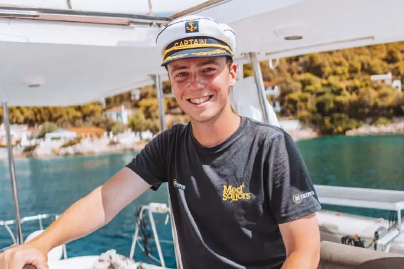 A young MedSailors skipper smiles while at the helm sailing guests to beautiful Mediterranean bays.