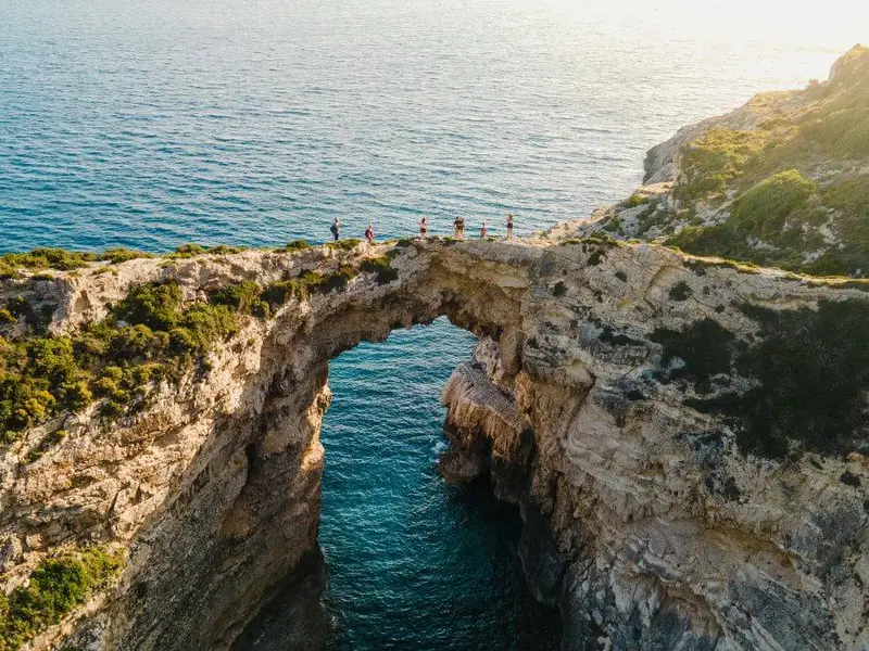 A breathtaking view of a natural rock arch over the Ionian Sea, showcasing Greece’s best outdoor adventure spots, from cliff jumping and snorkelling to scenic coastal hikes.