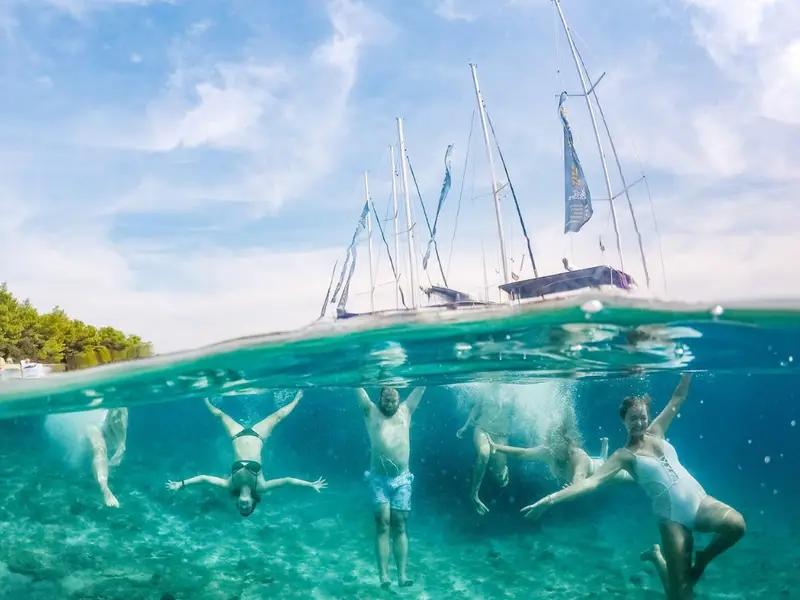 Travellers swimming underwater during a sailing swim stop near yachts in clear blue water along the Croatian coast.