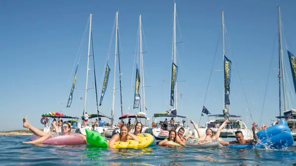 People on floaties in front of a raft of yachts
