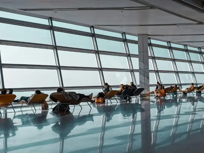 Travellers and backpackers resting in an airport lounge during a travel delay, highlighting a common part of Europe trips where flights or connections can be disrupted. This image reflects real travel scenarios such as delayed flights, missed connections, and waiting periods, which are key reasons travellers consider travel insurance for Europe. Ideal for illustrating travel delays, airport experiences, and practical planning for backpacking trips across Europe.