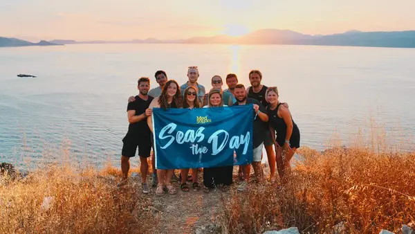 A group of young 20s and 30s travellers atop the acropolis of Hydra after a sunset hike from Hydra Town, one of the best viewpoints in the Saronic islands, an activity included on a MedSailors island hopping tour from Athens..