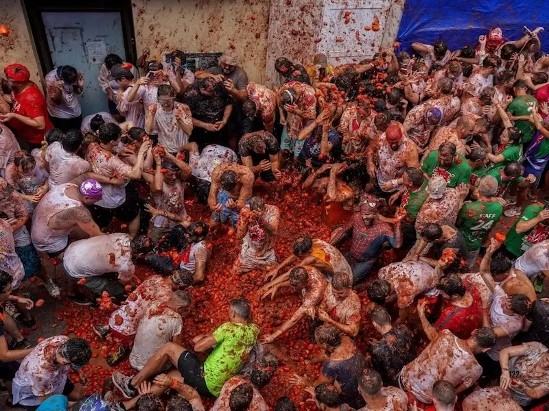 A massive crowd of travelers covered in crushed tomatoes at the La Tomatina festival in Buñol, Spain, featured in the MedSailors 2026 Europe festival guide.