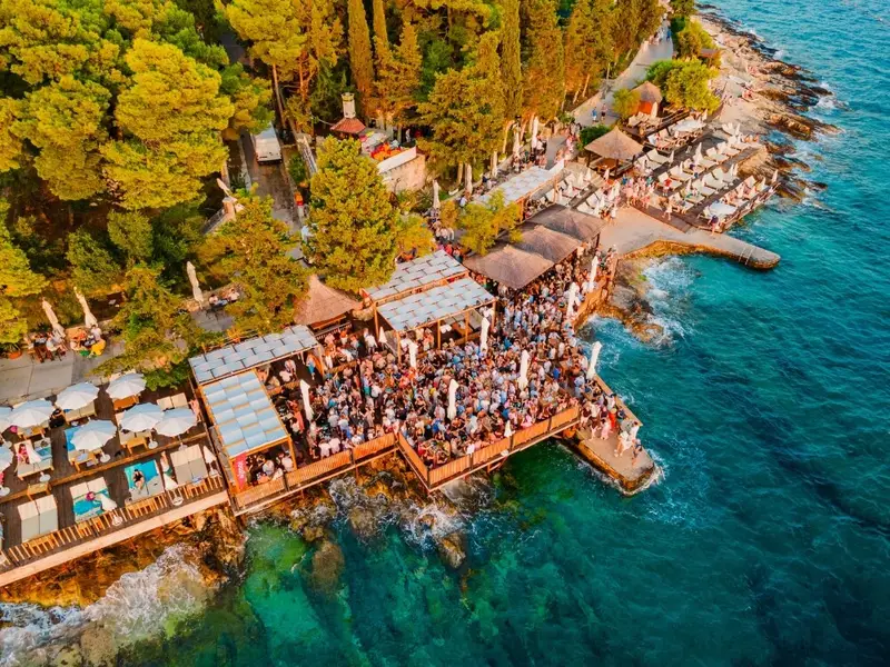 Aerial view of a busy waterfront beach club on the Croatian coast, showing the lively summer nightlife and social atmosphere Croatia is known for in August.