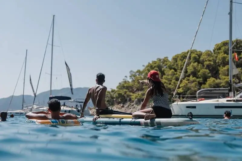 Travellers paddleboarding and relaxing on inflatables in a quiet turquoise bay on a MedSailors island hopping trip in Greece.