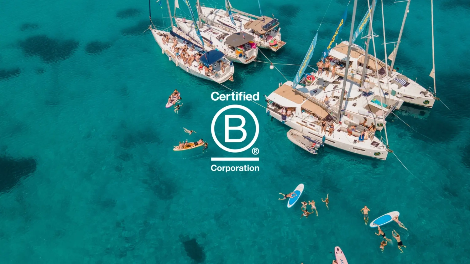 Aerial view of MedSailors sailing flotilla rafted together on turquoise Mediterranean water with guests swimming and paddleboarding, with Certified B Corporation logo overlay.