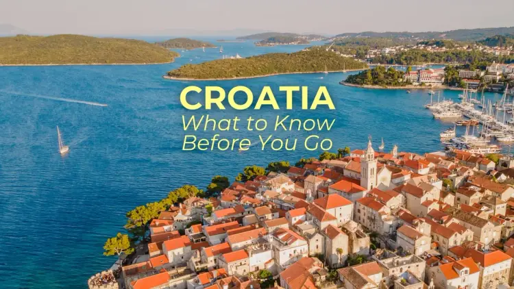 Aerial view of a historic Croatian coastal town and marina on the Adriatic Sea, showing islands, sailing boats, and red-roofed buildings.