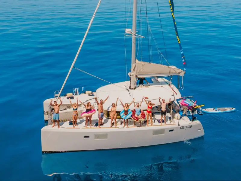 A group of young travelers in swimwear standing on the deck of a white MedSailors catamaran named 'Salty Dog' in the calm blue waters of the Mediterranean; showcasing the small group social atmosphere of sailing trips in Croatia and Greece.