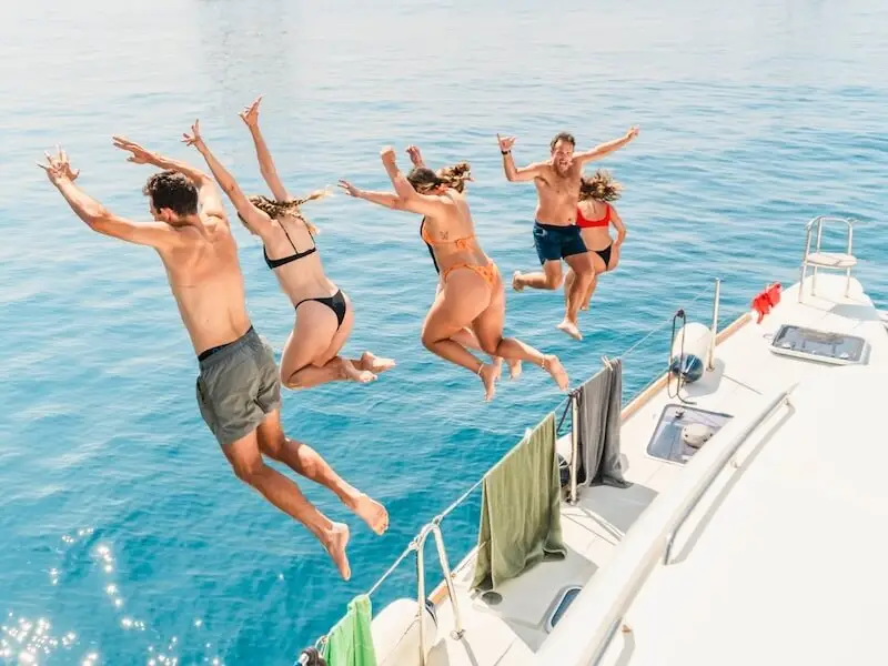 Group of young travellers jumping off a MedSailors yacht into clear blue water during a sailing holiday in Croatia or Greece — capturing the fun, adventurous spirit of an island-hopping trip in the Mediterranean.