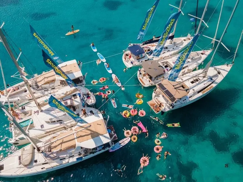 Aerial view of a Croatia yacht week party with MedSailors as guests swim, paddleboards and MedSailors boats tied together in Croatia with swimmers, paddleboard, and explore.