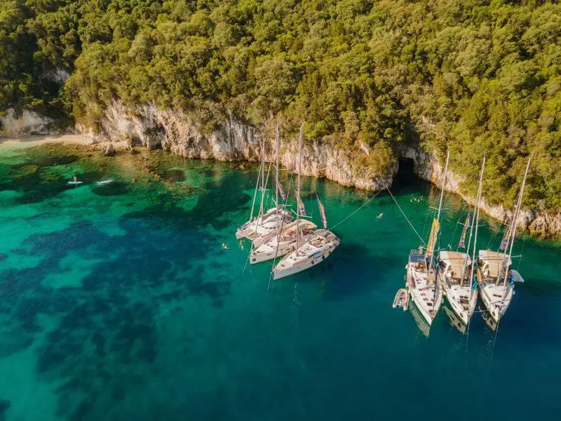 A fleet of yachts anchored in a hidden bay near Corfu, where travellers enjoy paddleboarding, snorkelling, and exploring Greece’s untouched island gems.