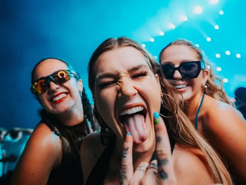 A group of friends laughing and posing at one of the best music festivals in Europe for 2026 during a MedSailors island hopping tour, featuring festival glitter and trendy sunglasses.