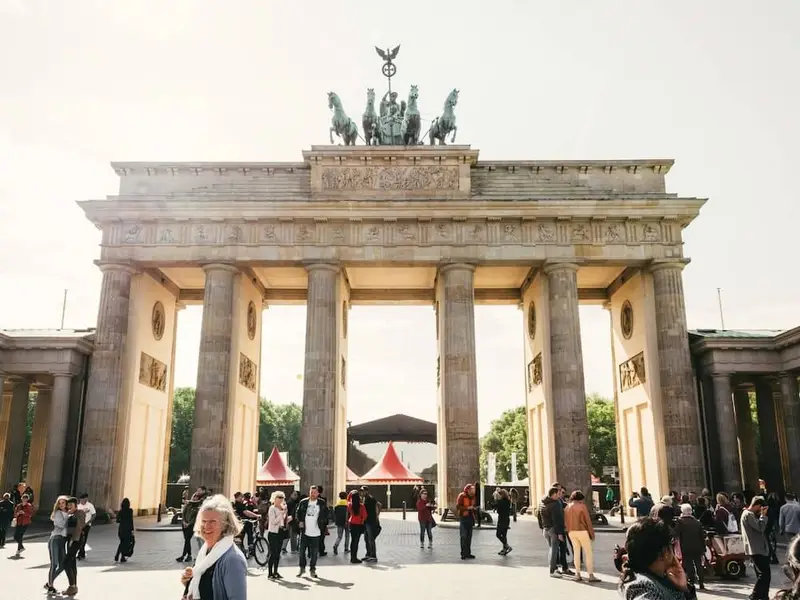 Crowds gather in front of the Brandenburg Gate in Berlin on a bright afternoon, with the neoclassical columns and the Quadriga statue visible on top. People walk, chat, and take photos in the open square, capturing Berlin’s iconic landmark and lively city atmosphere for first-time Europe travellers exploring history, museums, and nightlife.