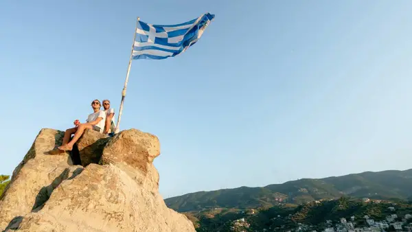 Two men sitting on a rock in Greece with the Greek flag