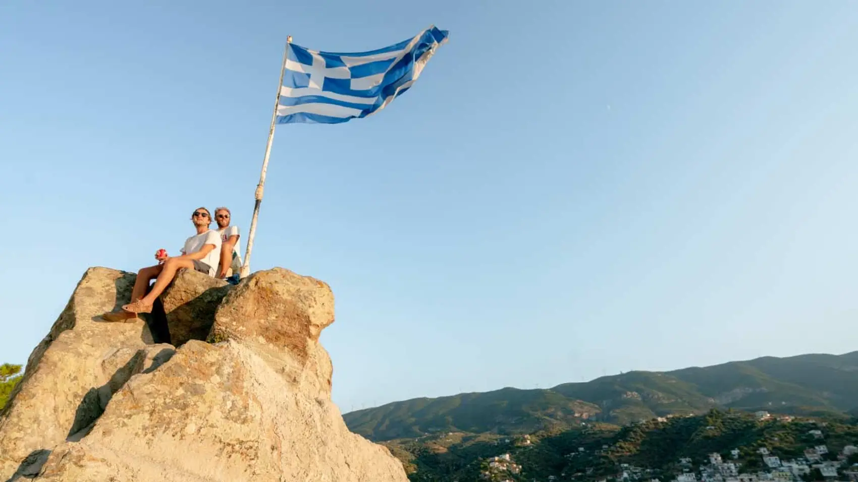 Two men sitting on a rock in Greece with the Greek flag