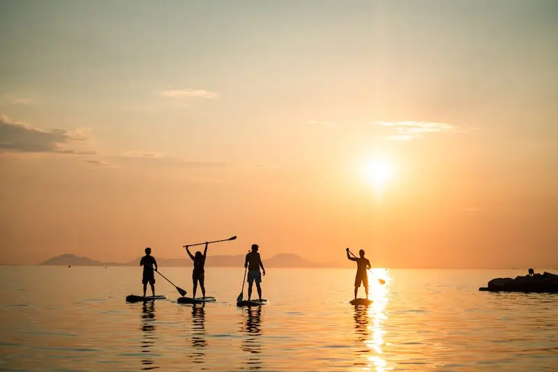 4 silhouettes of people paddleboarding into a golden sunset while on a MedSailors yacht week in Greece.