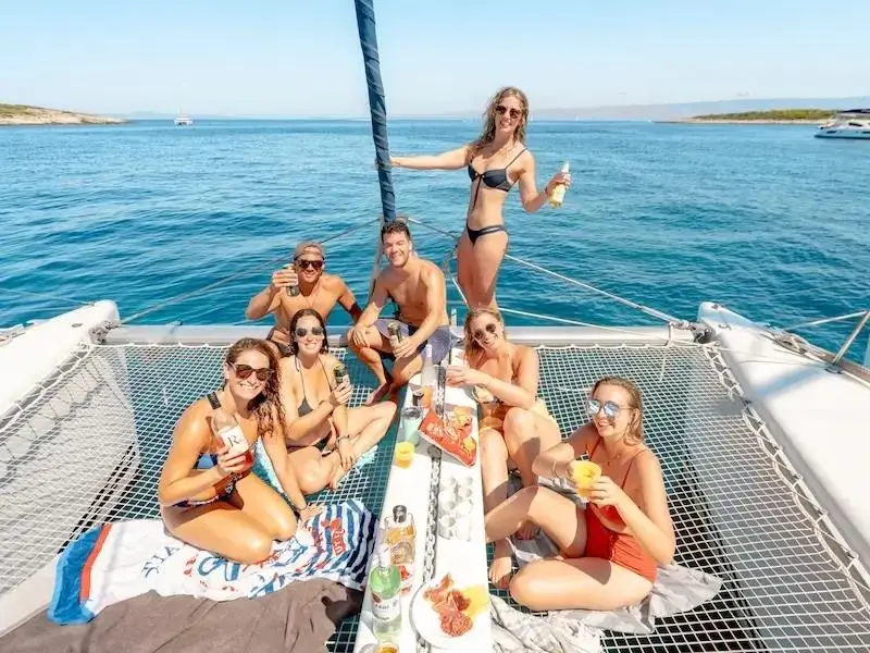 A group of 20-something travellers drink cocktails and wine on a catamaran in the Mediterranean while they party on the yacht. 