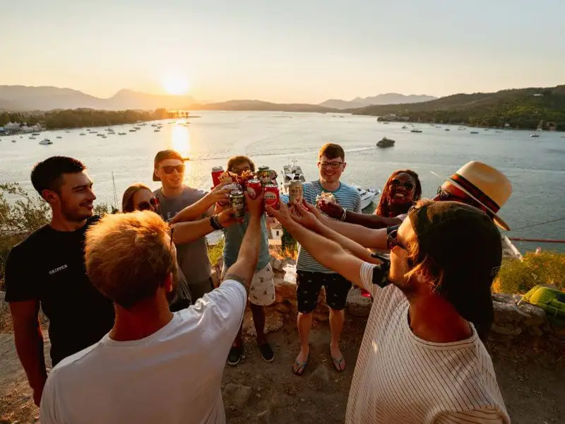 A group of friends raising their drinks at sunset, enjoying the lively party scene on a Greek island-hopping adventure, featuring top destinations like Poros.