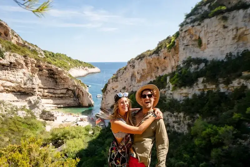 Happy couple exploring Stiniva Cove on Vis Island, during a MedSailors sail week in Croatia, surrounded by dramatic cliffs, turquoise water, and lush greenery.
