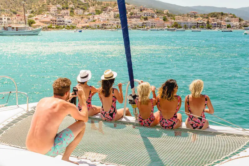 People sitting on the front of the catamaran on a Greece yacht week with MedSailors, all wearing matching outifts. 