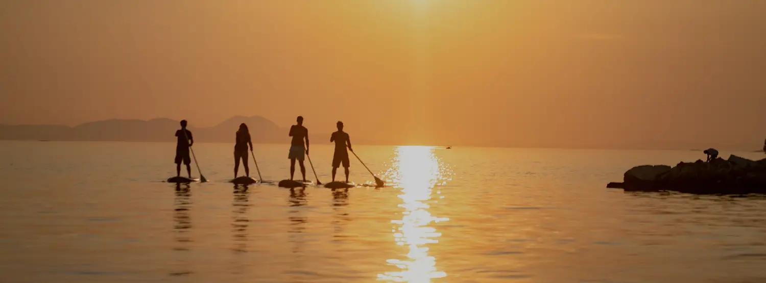 Group of people paddle boarding during sunset in Greece