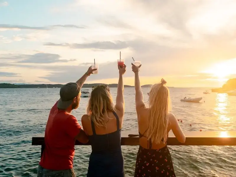 Three young travellers party at a seaside bar in Paxos Greece that is a better alternative to Mykonos and Ios for backpacker nightlife.