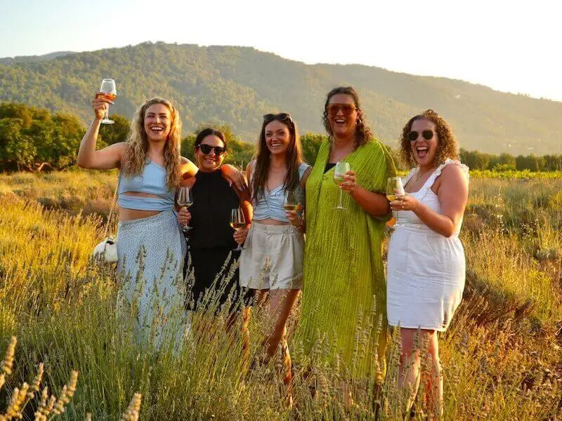 Group of MedSailors travellers enjoying wine at Hora Farm on Hvar Island, Croatia, standing in a vineyard during golden hour with mountains in the background.