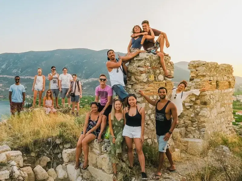 A group of young backpackers sit atop Greek ruins at sunset while on a budget adventure tour of Greece with MedSailors.