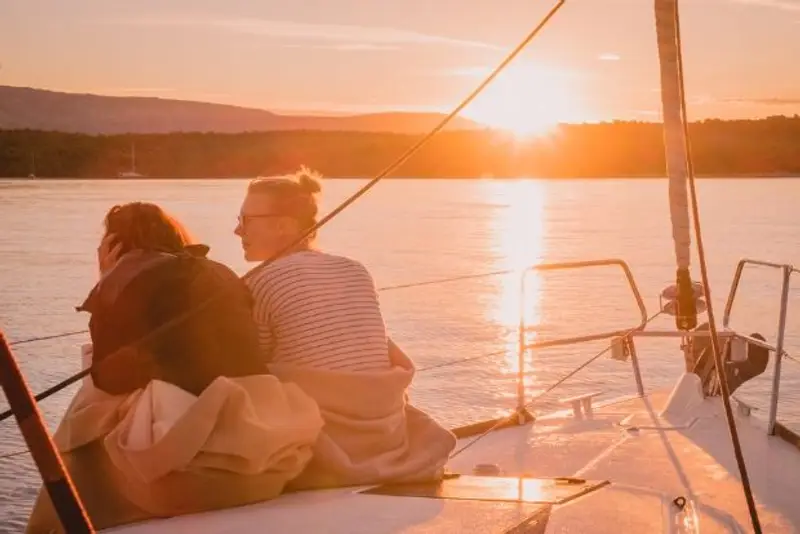 Two females sit on the bow of a sailing yacht watching a beautiful golden sunrise.