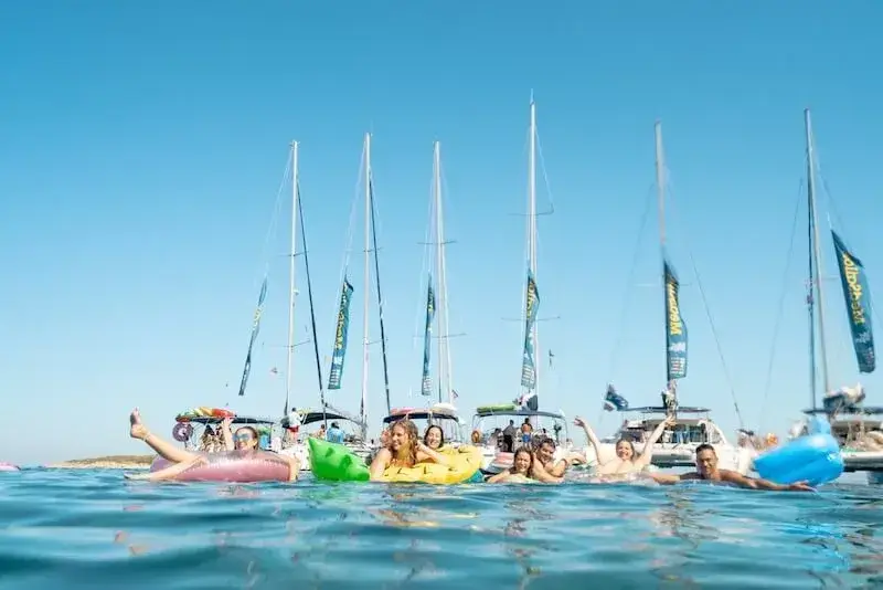 MedSailors sailing holiday guests floating on inflatables in crystal-clear water with yachts anchored behind, island hopping in Croatia under sunny blue skies.