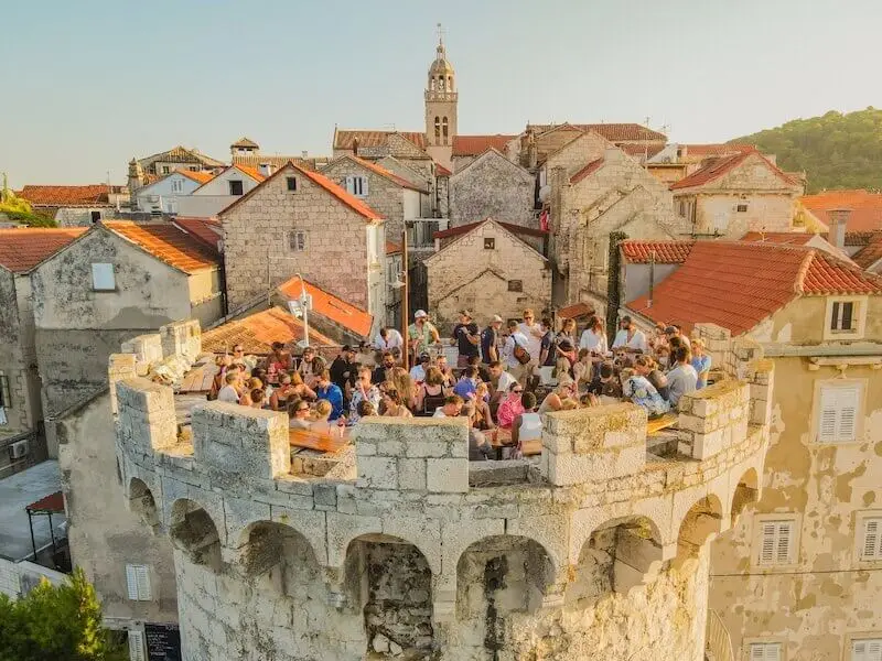 Crowd of MedSailors guests enjoying cocktails at Massimo’s rooftop bar in Korčula, Croatia, perched on a medieval stone turret with views over the old town.
