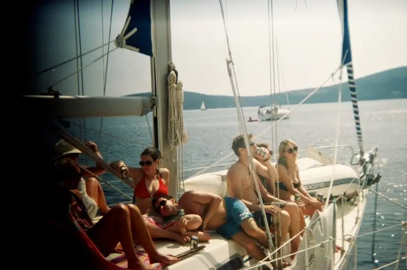 A group of Aussie and Kiwi travellers celebrate together on a yacht week in Croatia with MedSailors holding bottles of alcohol.