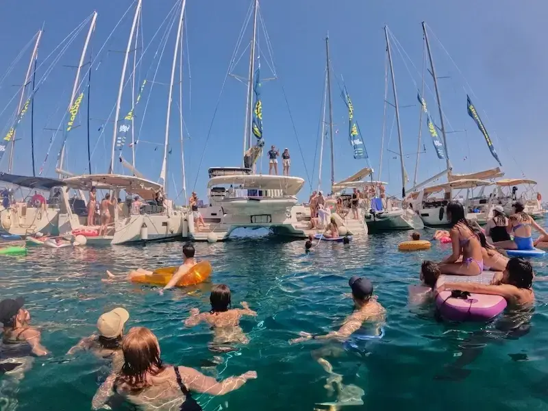 Group of yachts and people swimming in crystal clear waters of Greece while on a budget Greek island hopping trip with MedSailors.