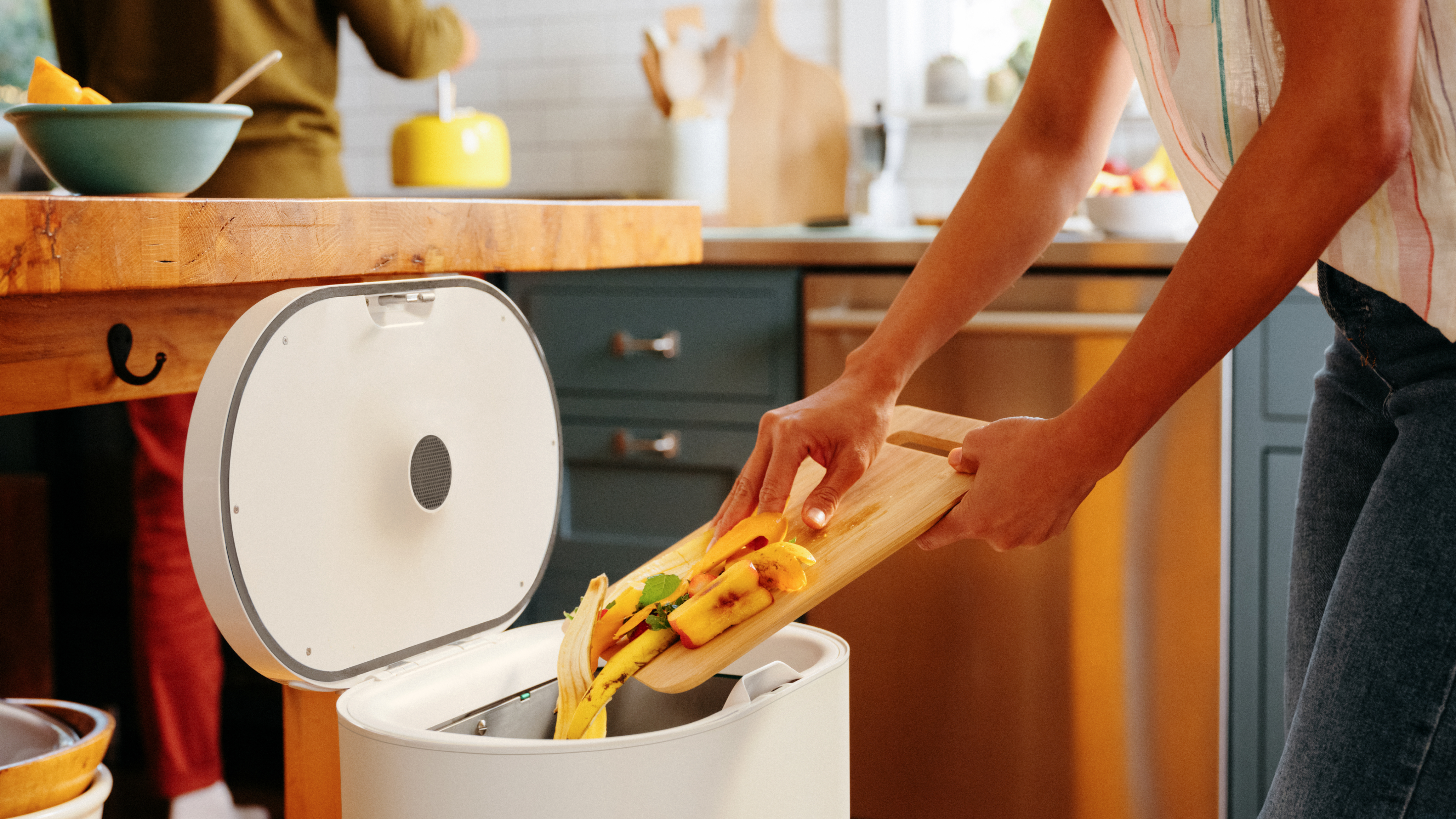 A person moving  kitchen scraps from a cutting board into a Mill kitchen bin.