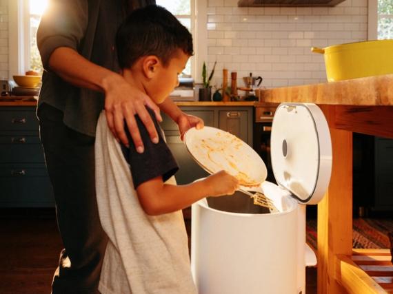 A family emptying kitchen scraps into their Mill kitchen bin, instead of putting them into a trash can.