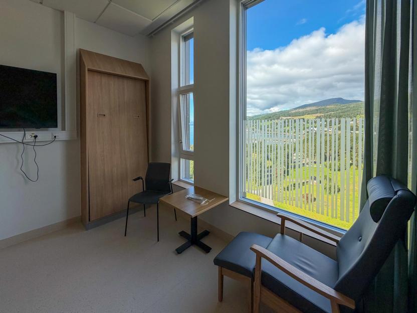 Pasientseng i rom som har tv plassert i mot senga og delvis folierte vinduer i nedre felt.
