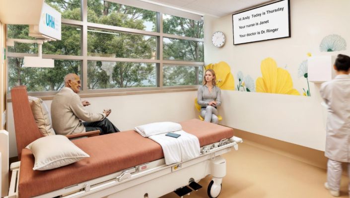 Foto viser en eldre pasient som sitter ved vinduet i et enerom. På veggen er det en informasjonsskjerm som pasienten kan lese.