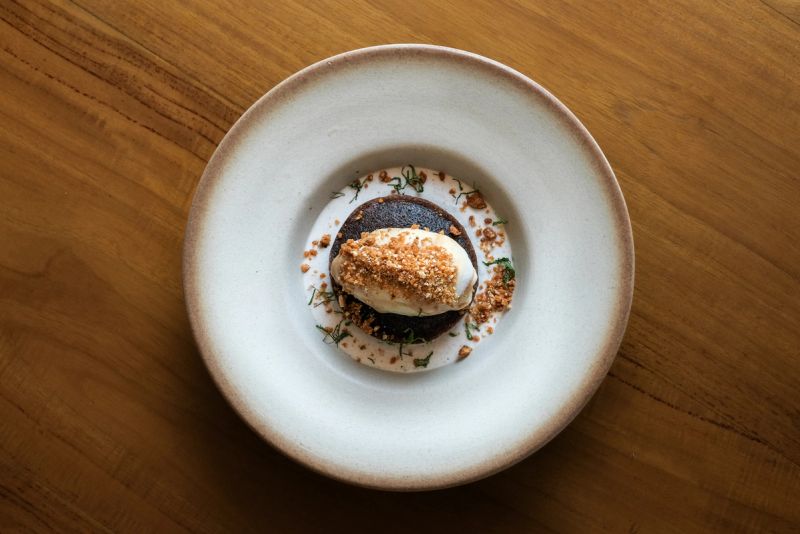 Black rice pudding topped with ice cream in a white bowl on a wooden table.