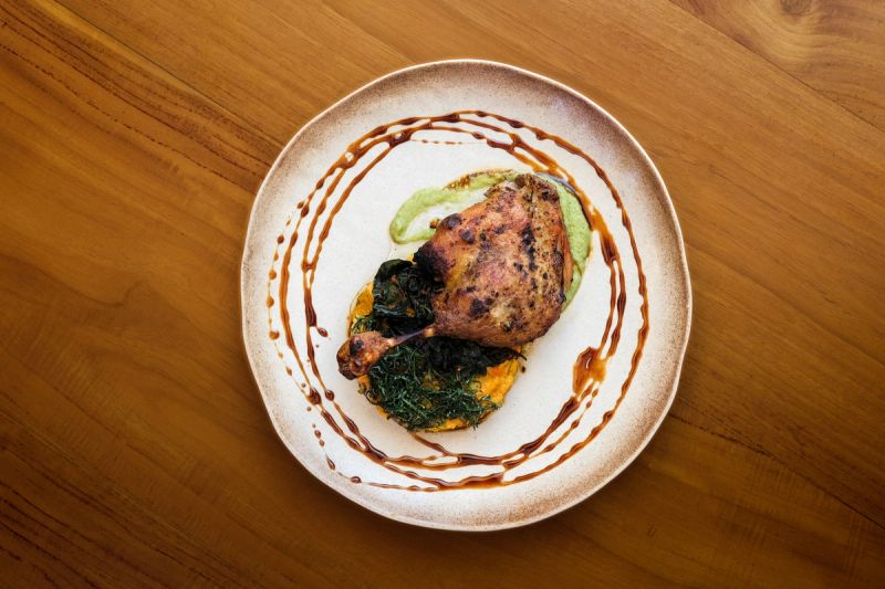 A plated poultry dish with greens and sauce on a wooden restaurant table.