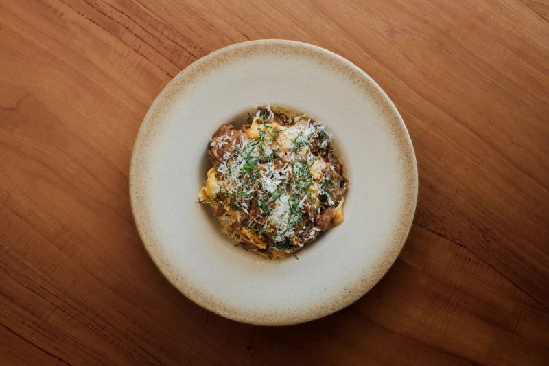 Fresh pasta with beef ragu and grated cheese, served in a wide ceramic bowl.