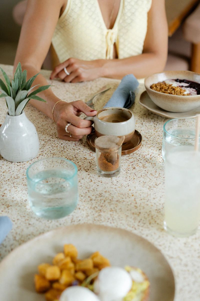 A guest holding a coffee cup beside a breakfast bowl at Boni Beach.