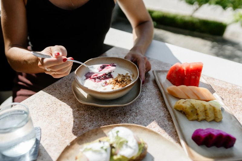 A breakfast bowl with granola and a fresh fruit plate on a restaurant table.