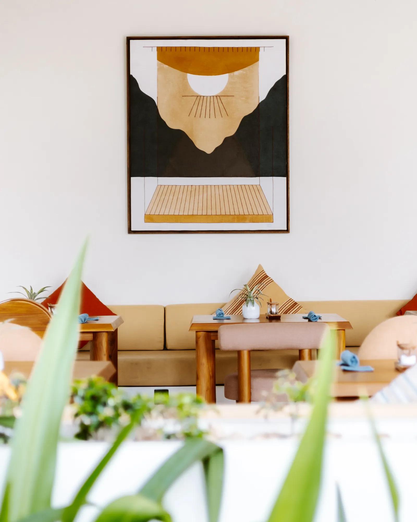 Framed artwork above cushioned seating and teak dining tables in the Boni Beach restaurant.