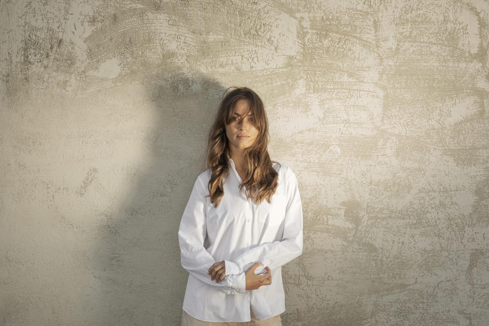 Photo of Woman posing in front of wall with long hair and white shirt