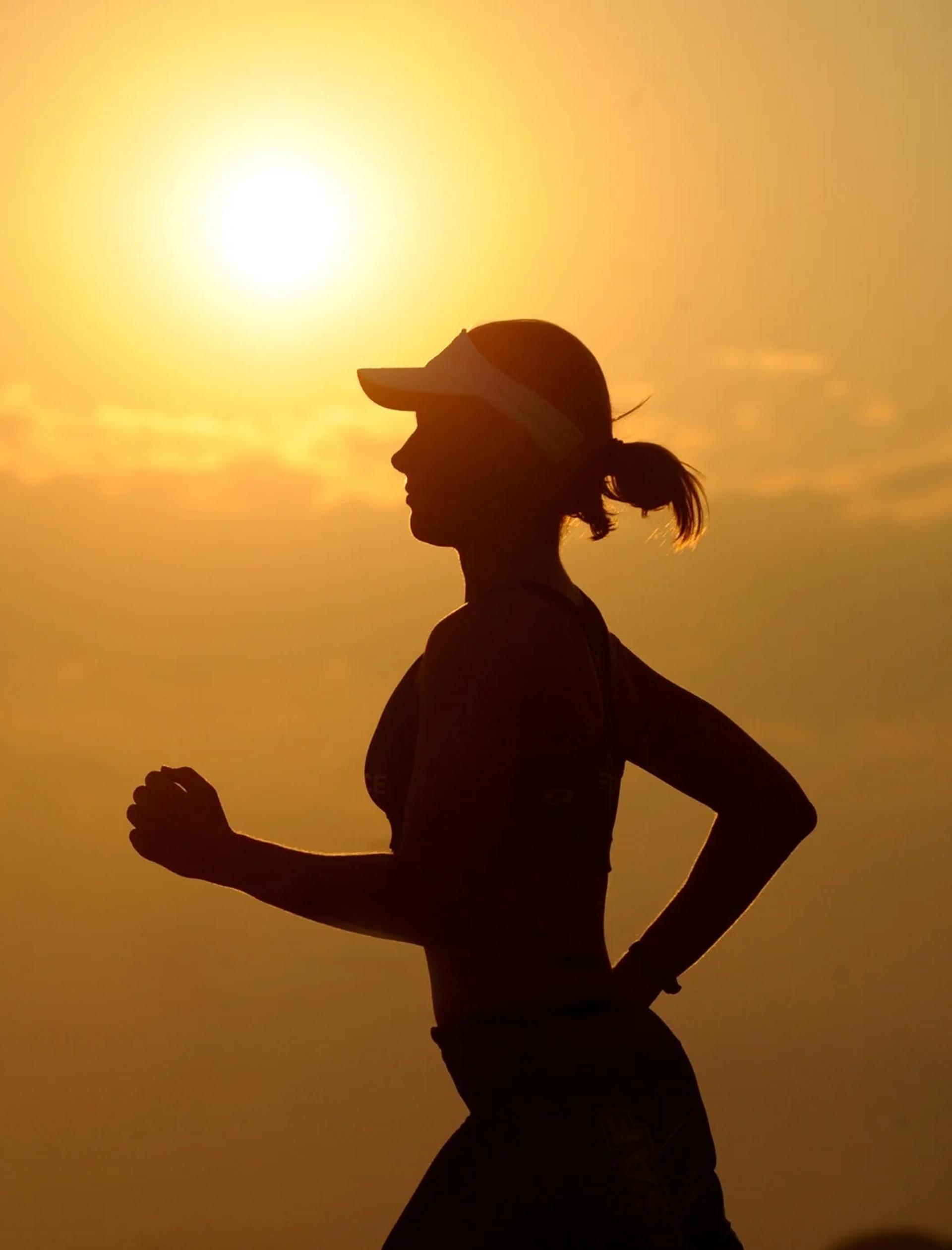 A woman in a visor running of jogging past a sunset