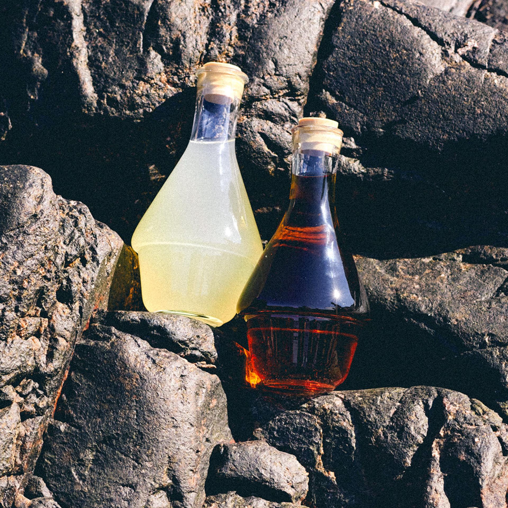 Two glass containers filled with Extract ingredients resting on rocks