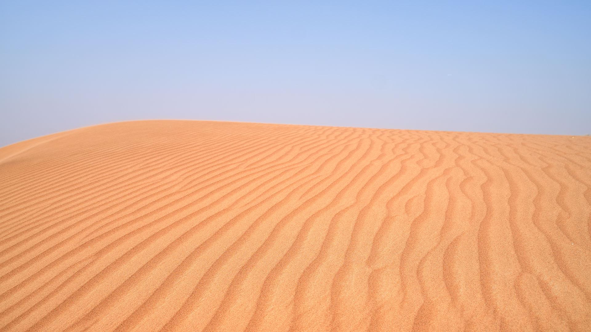 Image of a golden desert sand dune with a ripple effect pattern creating waves in the sand