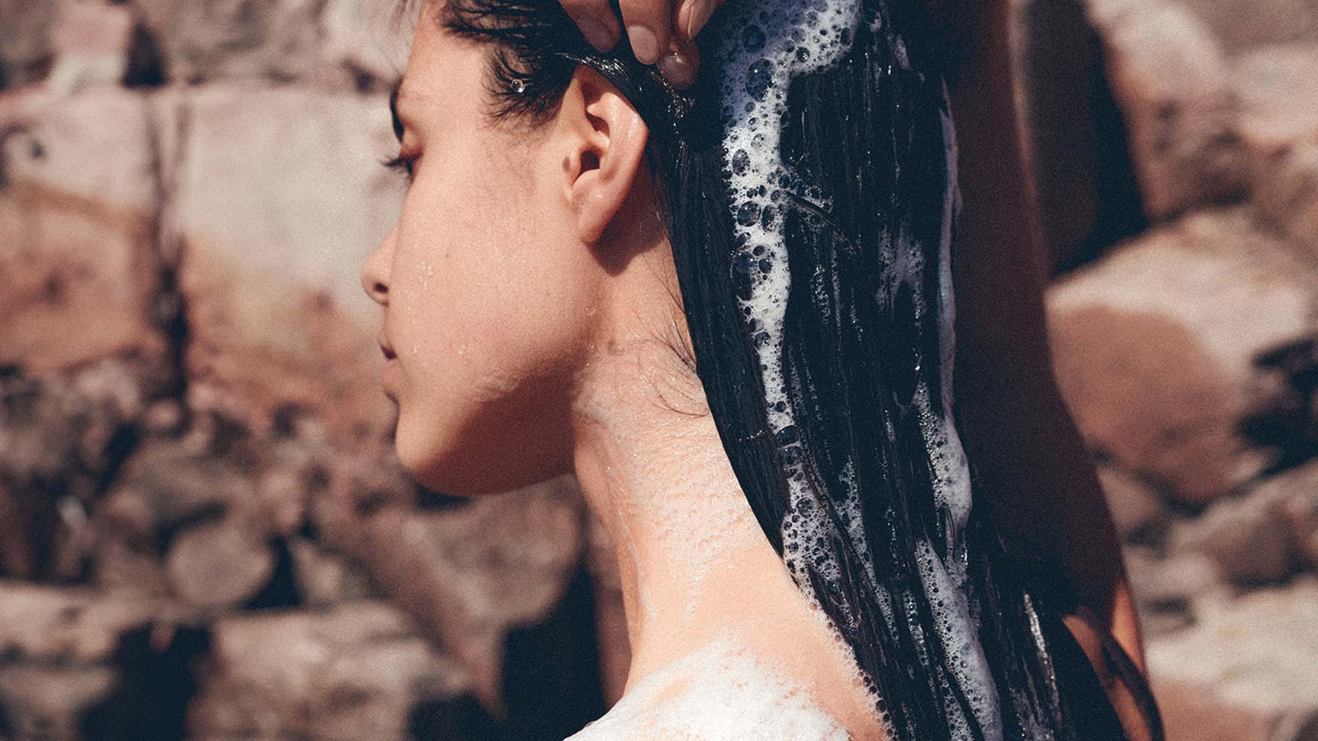 Woman washing hair with shampoo suds still at back of the head next to red rocks side angle